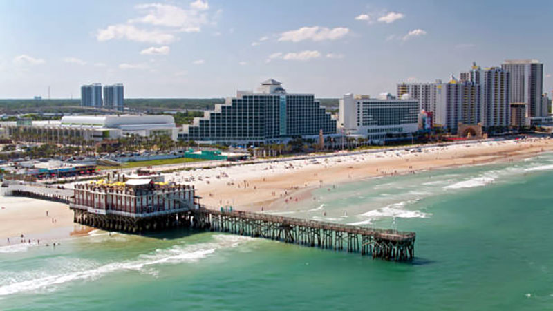 Aerial view of the pier and beachfront in Daytona Beach, Florida, with ocean waves and sandy shoreline Aerial view of the pier and beachfront in Daytona Beach, Florida, with ocean waves and sandy shoreline